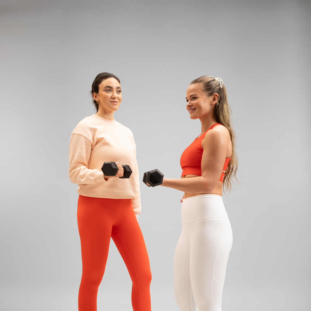 Zwei Gymondo-Trainerinnen in weiß-roter Sportkleidung und Joga-Leggings mit jeweils einer Kurzhantel in der Hand