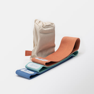 Booty Bänder in blau, türkis und orange mit Gymondo-Logo und Stofftasche mit Gymondo-Logo vor neutralem Hintergrund